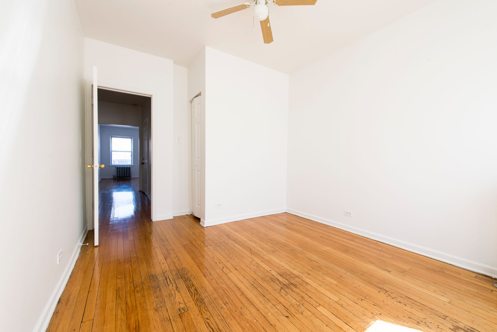 Empty room with hardwood floors, white walls, and an open doorway.