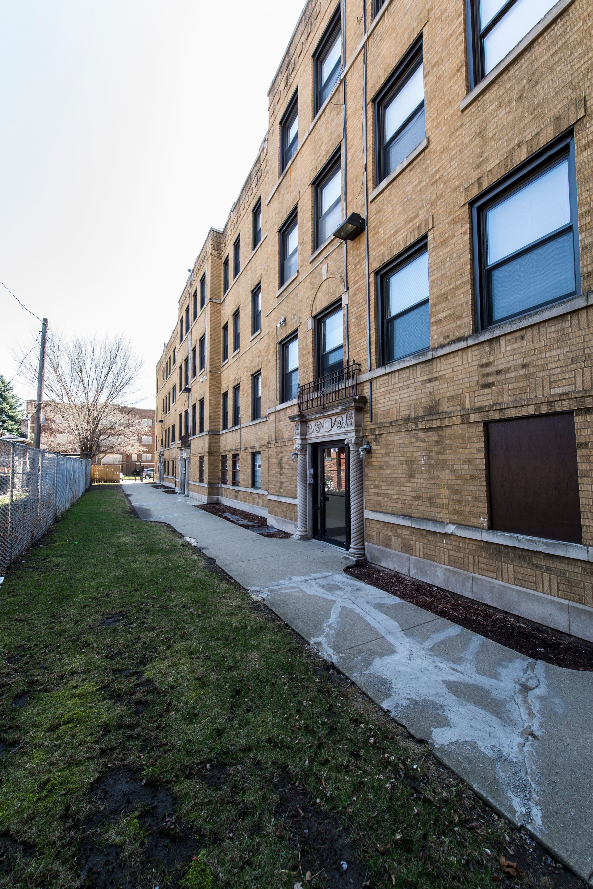 Brick apartment building with concrete walkway and grass.