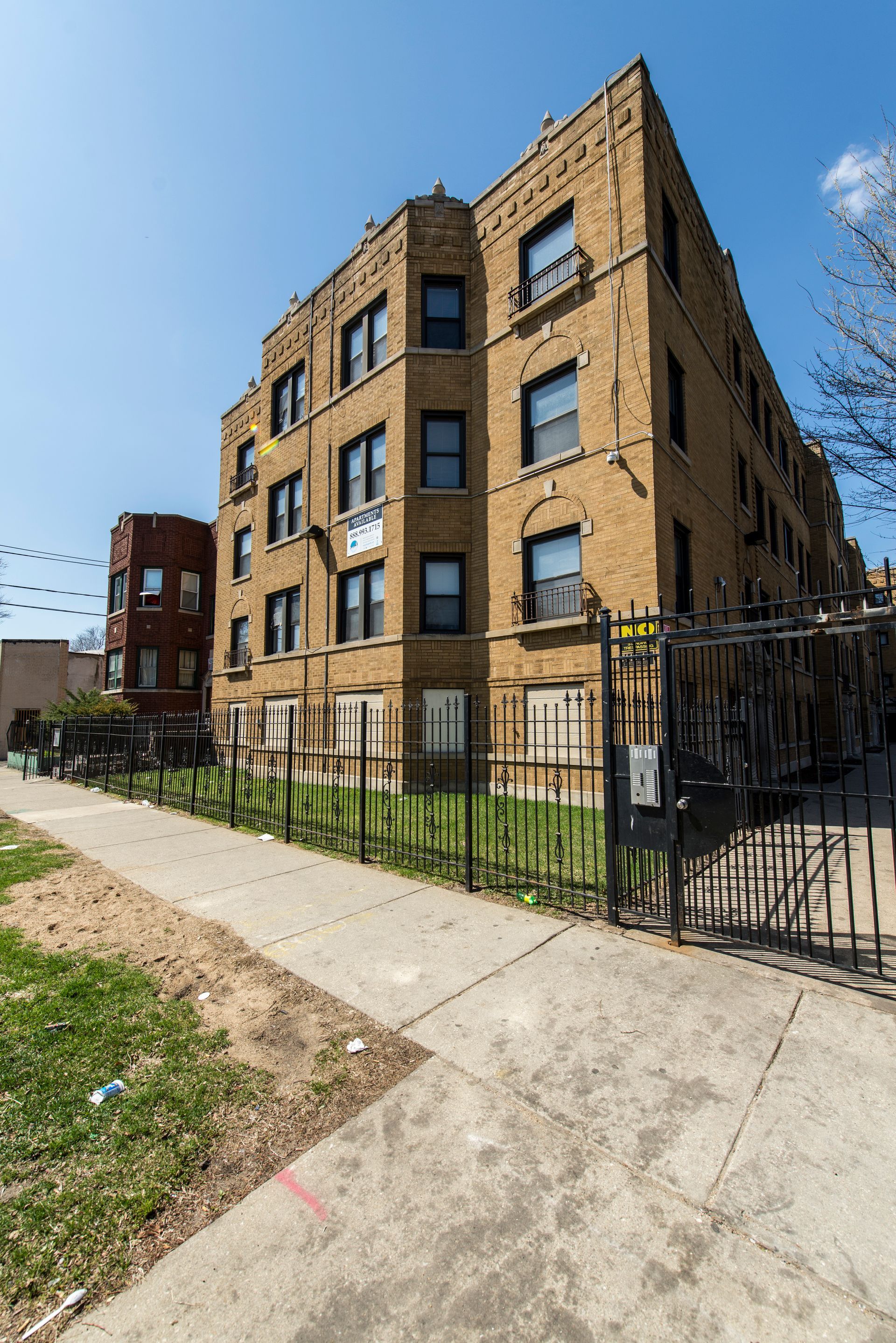 Brick apartment building behind a black fence on a sunny day.