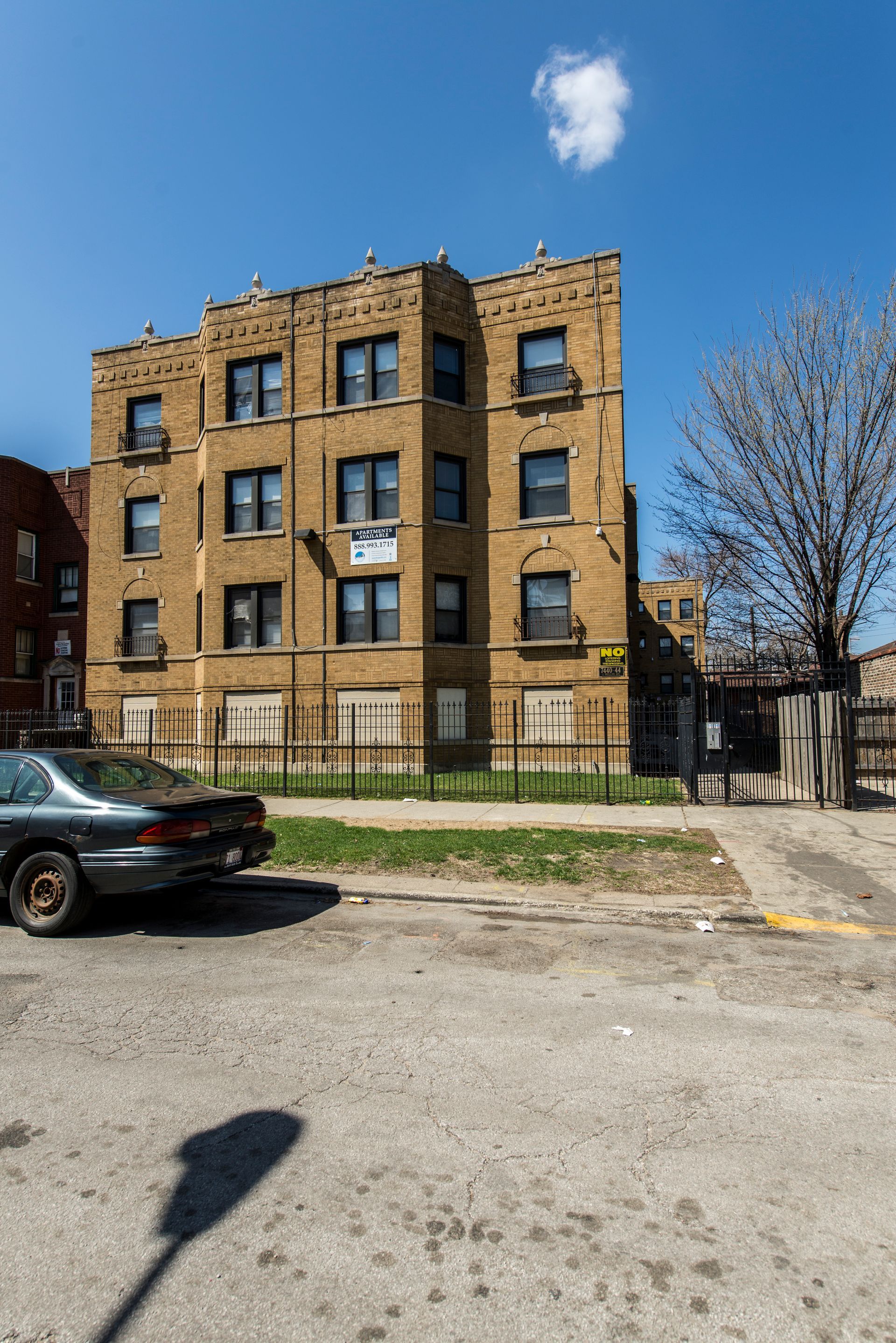 Tan brick apartment building under a blue sky, with a car in front.
