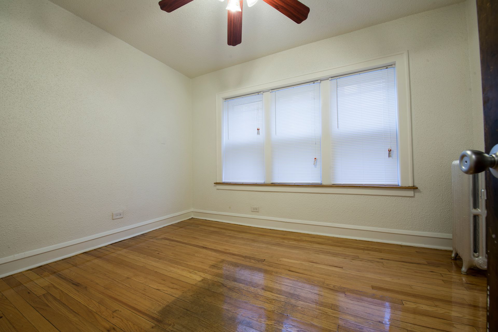 Empty room with hardwood floors, a window with blinds, and a ceiling fan.