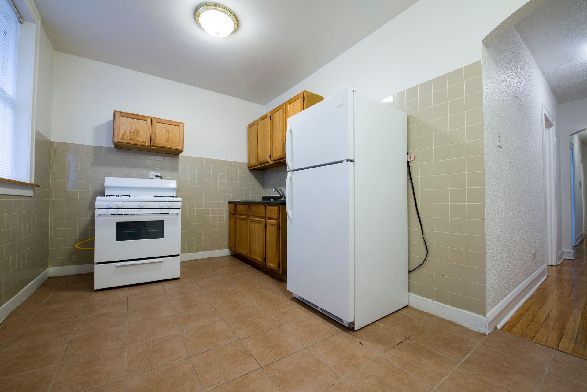 Small kitchen with tile backsplash, appliances: stove, refrigerator, wooden cabinets, and tan flooring.