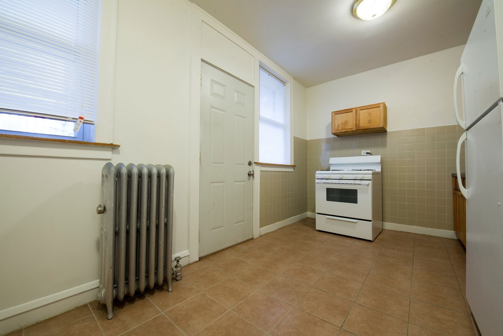 Small kitchen with a white stove, refrigerator, cabinets, and a radiator.