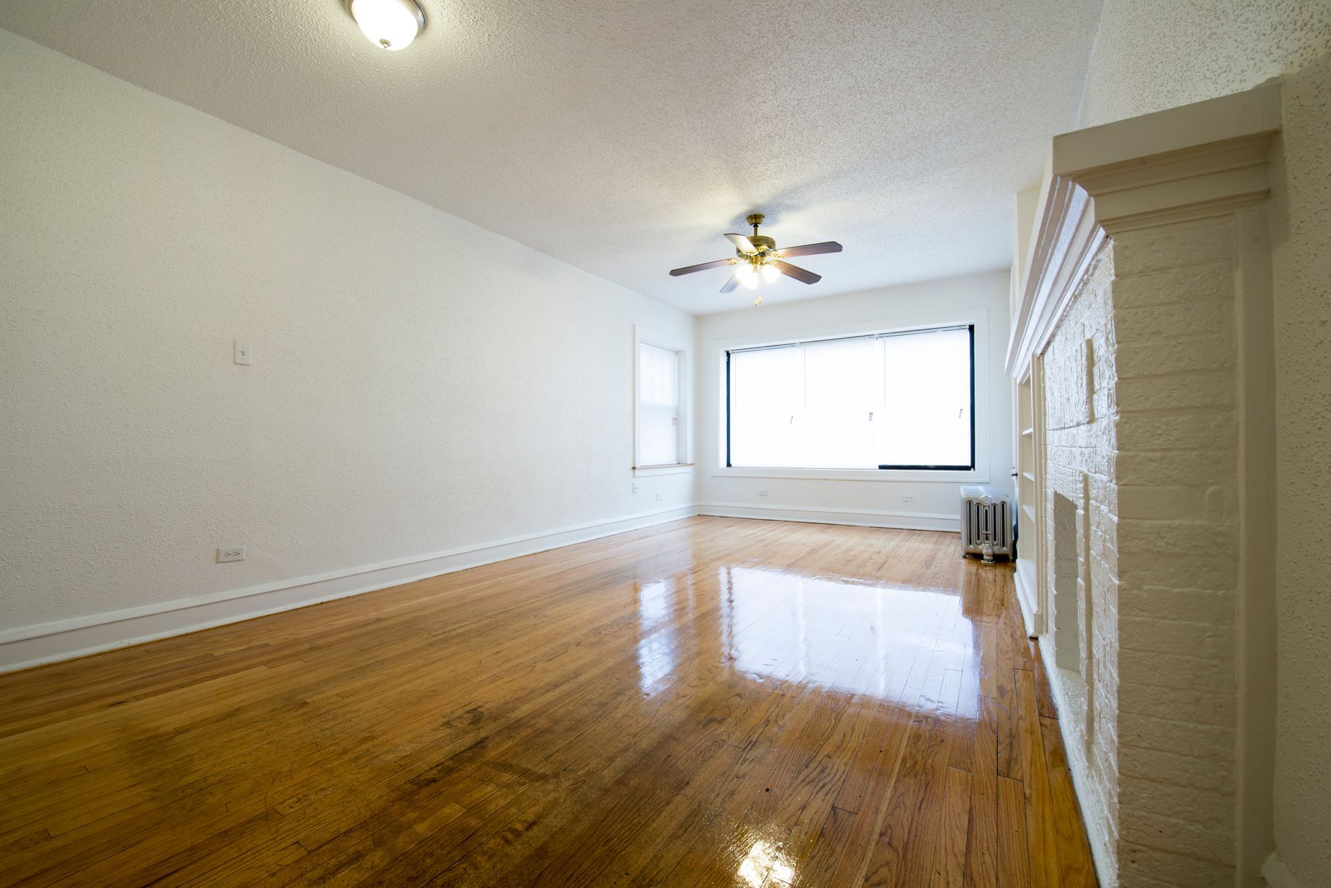 Empty living room with hardwood floors, white walls, and a window.