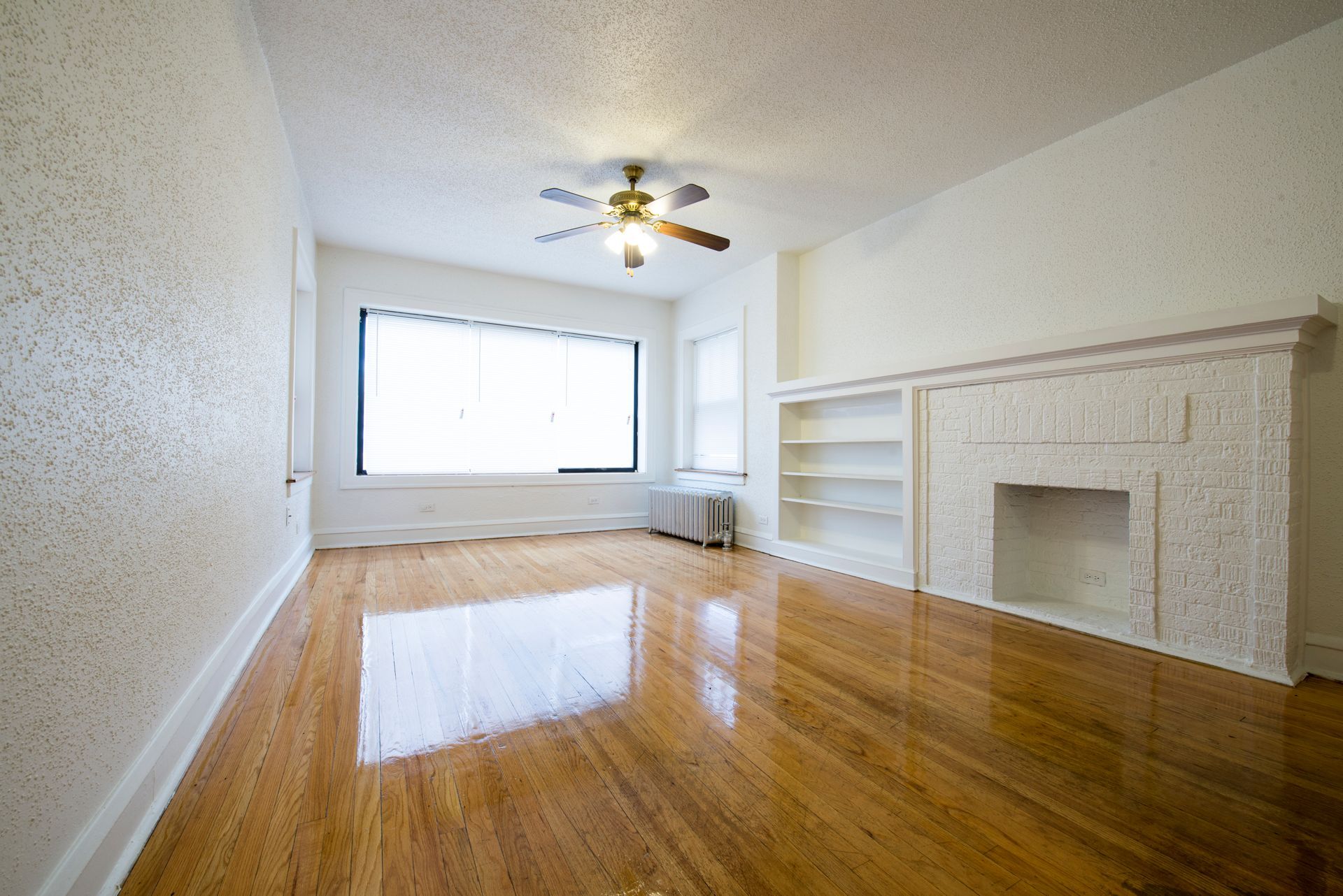 Empty living room with wood floors, fireplace, and large window.