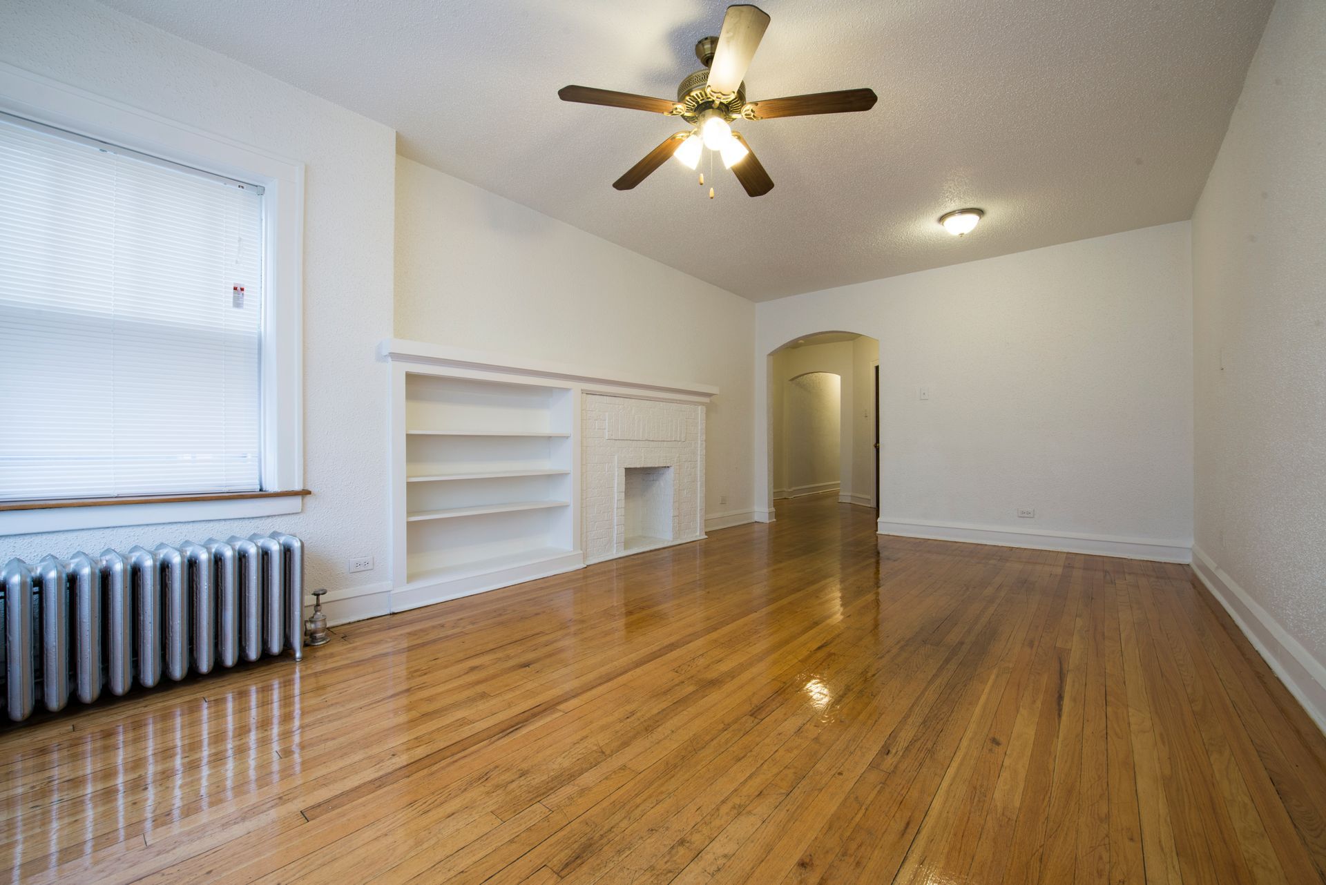 Empty room with hardwood floors, built-in shelves, and a ceiling fan.