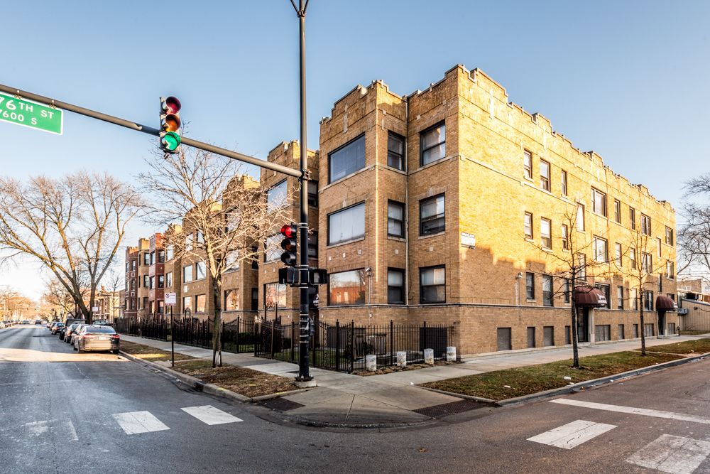 Multi-story brick apartment building at an intersection with a traffic light. Cars parked on the street.