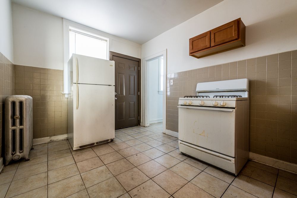 Kitchen with white appliances, brown cabinets, tan tiled walls and floor.