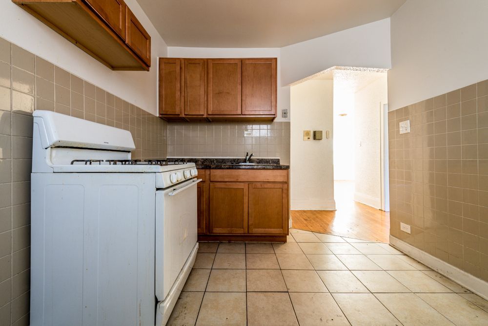 Kitchen with white appliances, brown cabinets, tile backsplash and flooring, and doorway to another room.