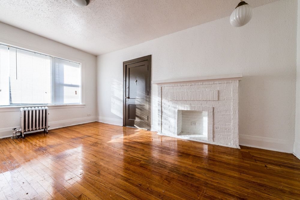 Empty room with hardwood floors, a white fireplace, and a window with blinds.