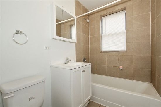 Bathroom with white toilet, vanity, and tub, beige tile, and a window with blinds.