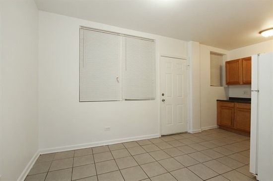 Empty kitchen with tile floor, window with blinds, door, and cabinets.