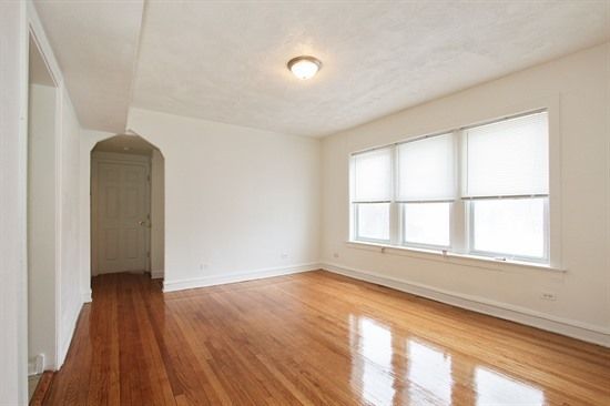 Empty room with hardwood floors, white walls, arched doorway, and a window with blinds.