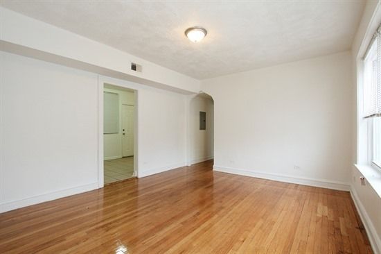 Empty room with hardwood floors, white walls, and a doorway.