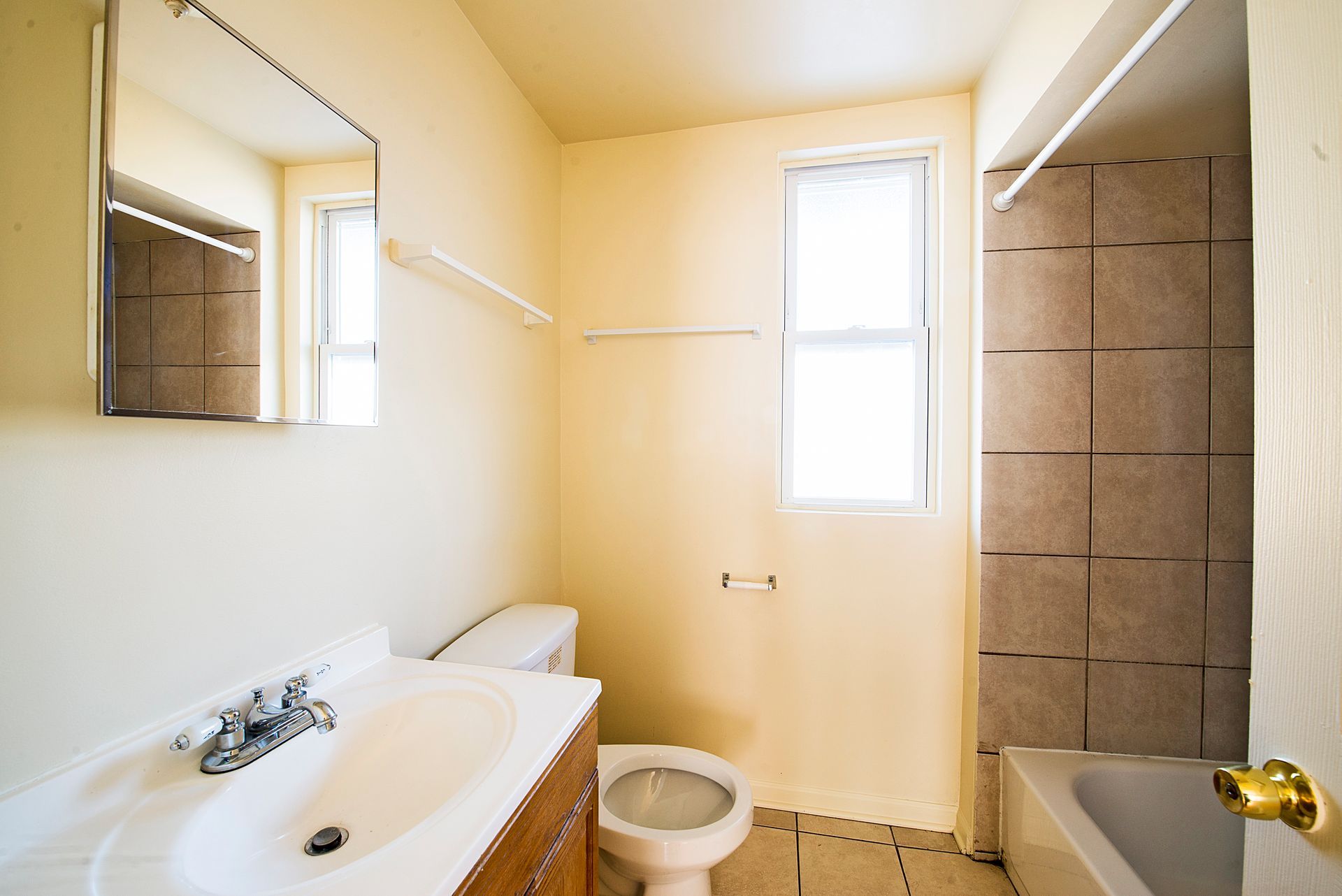 Empty bathroom with beige walls, a white sink, toilet, and bathtub with tile surround.