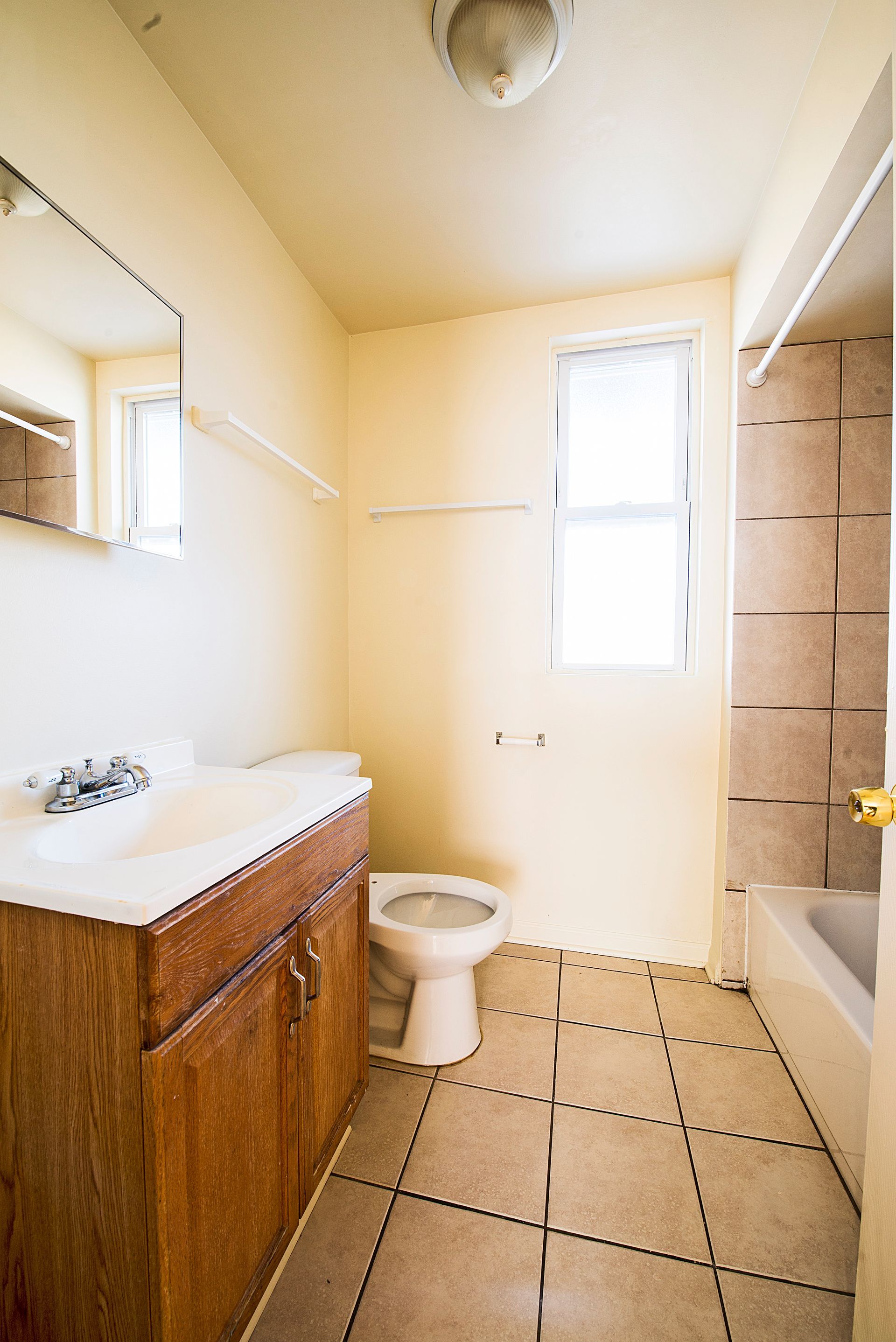 Bathroom with wood vanity, white toilet, window, and tiled floor and shower surround.