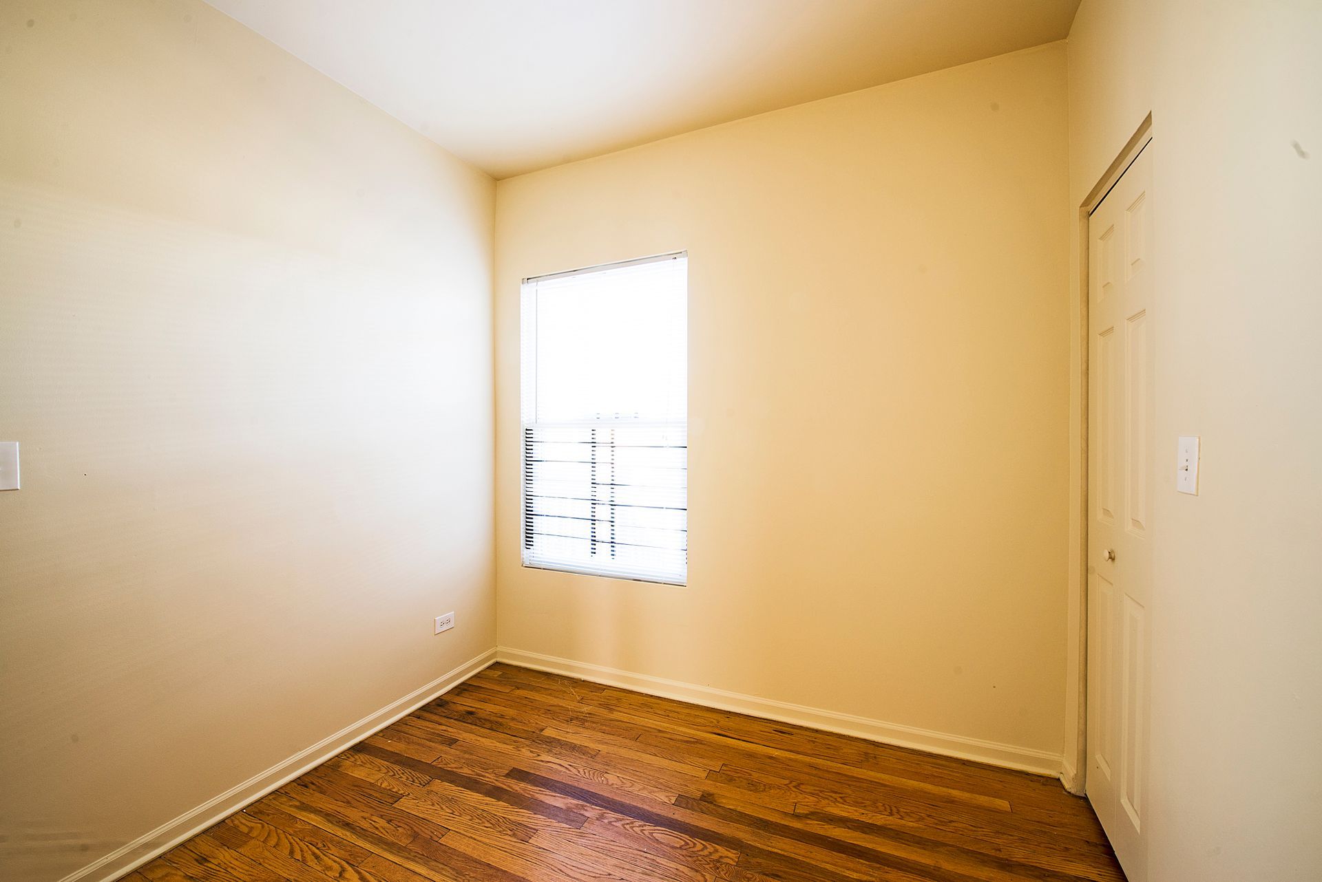 Empty room with hardwood floors, a window, and a closed door.