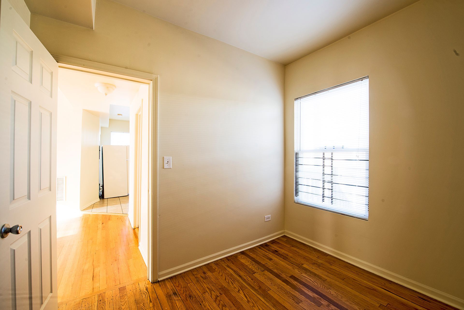 Empty room with hardwood floors, a window, and a doorway leading to another room.