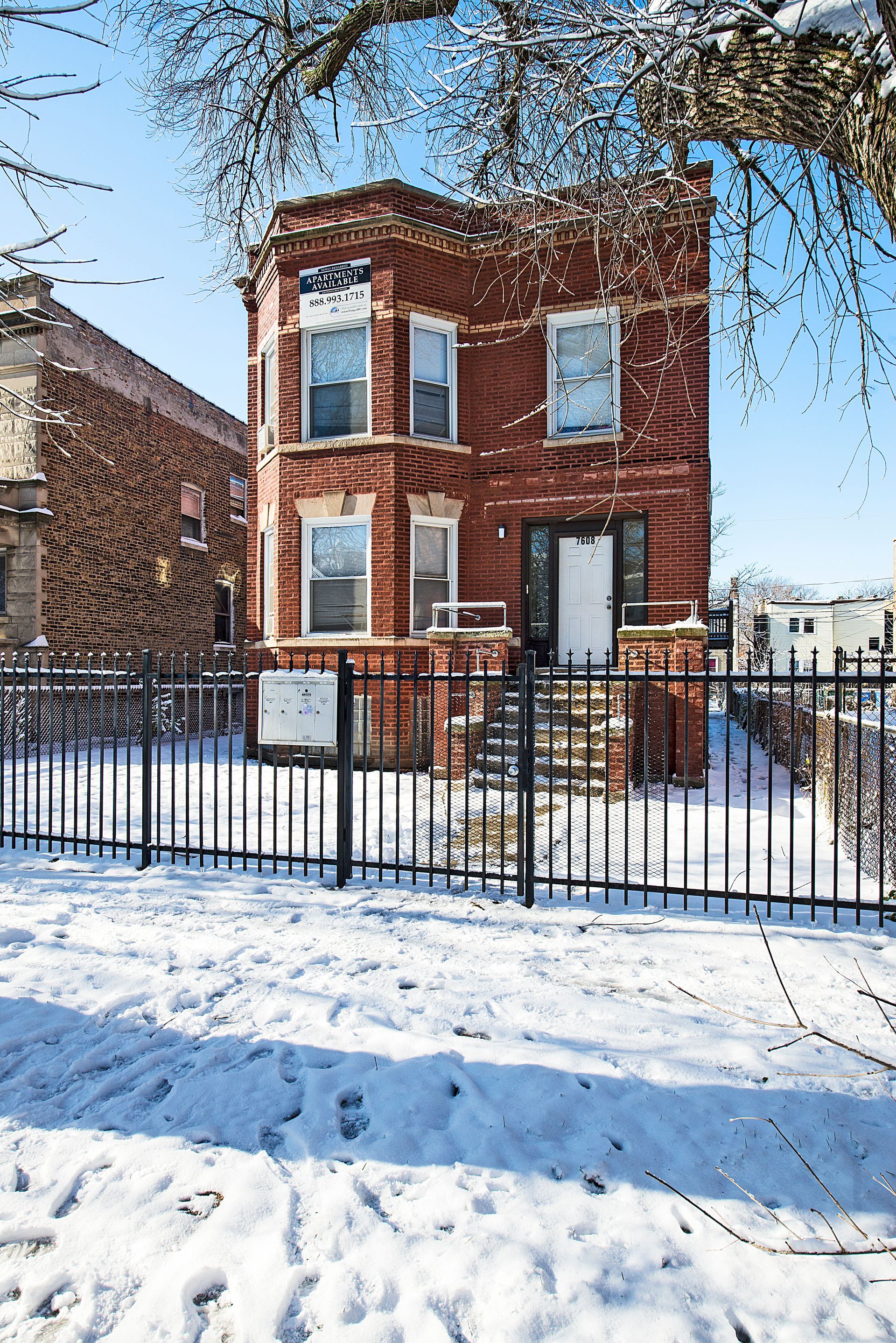 Brick house with snow-covered yard behind a black metal fence, on a sunny winter day.