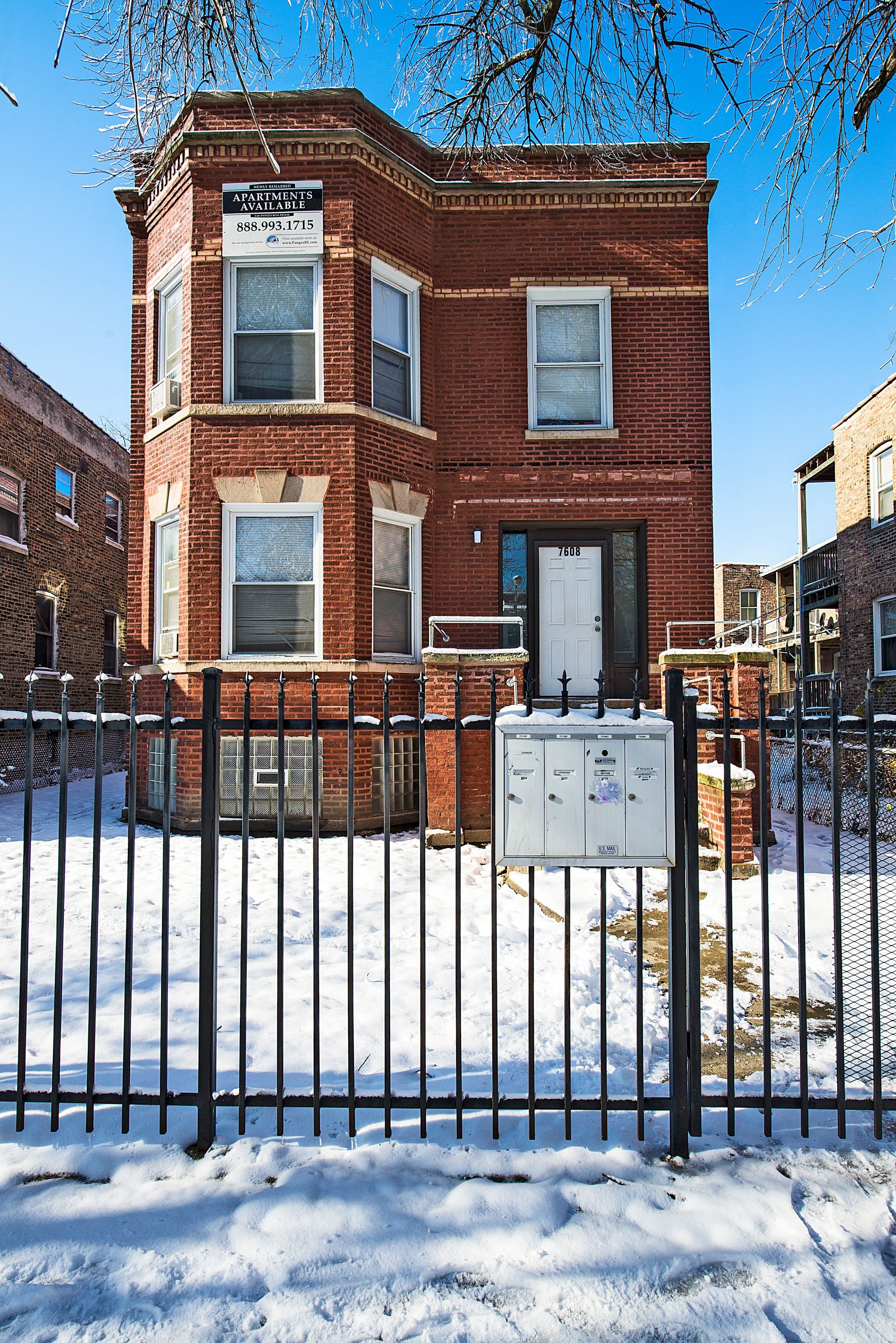 Brick two-story building behind a wrought-iron fence on a snowy day.