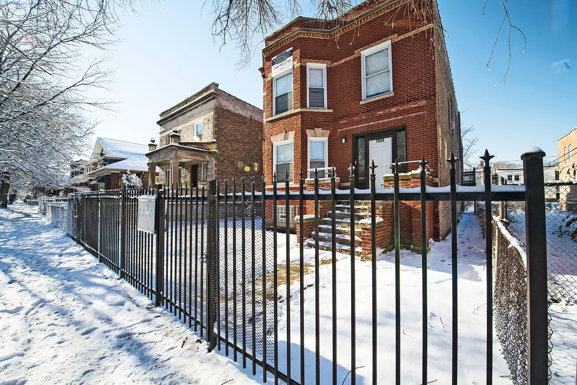 Brick house behind black fence, snow-covered ground, winter setting.