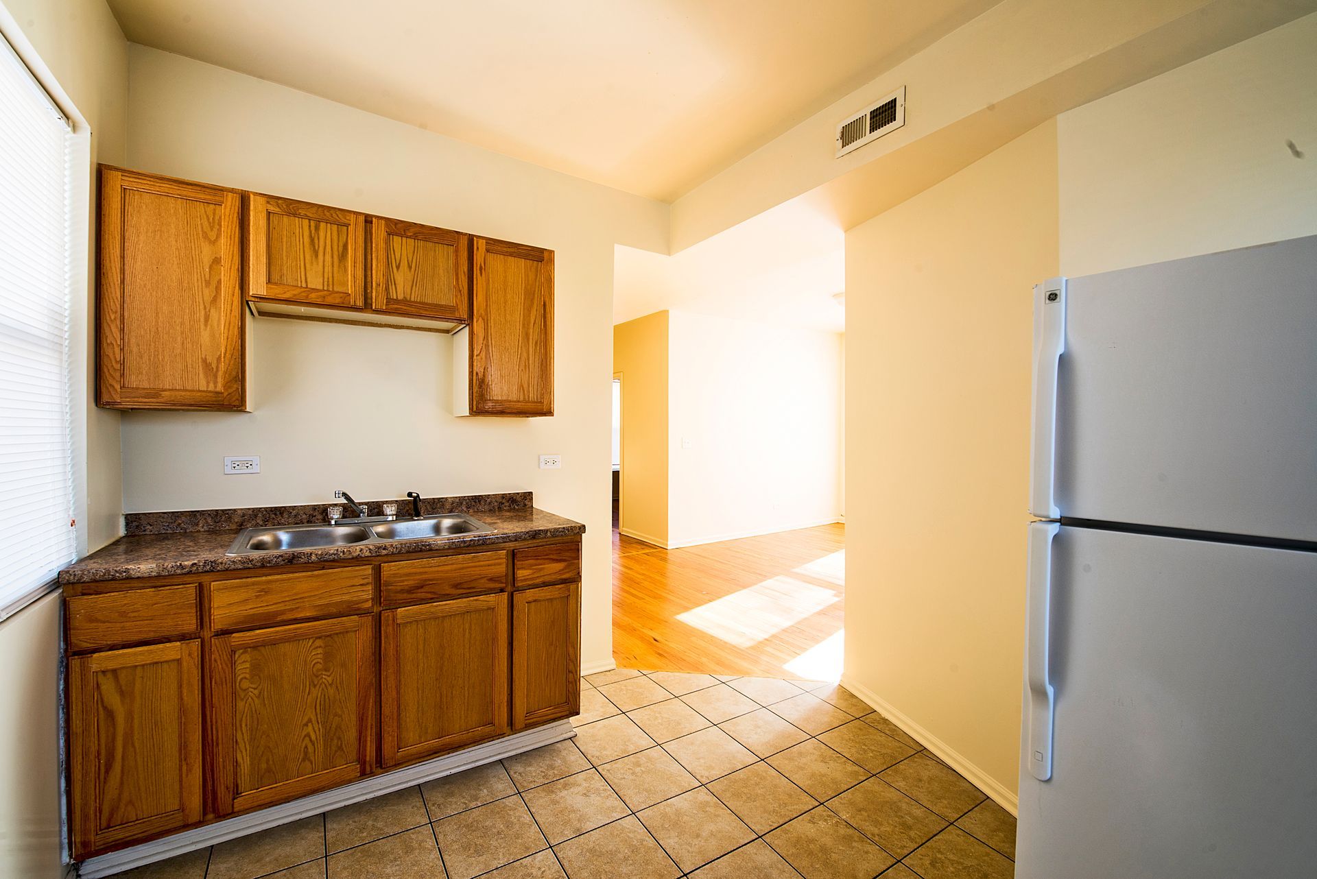 Kitchen with wooden cabinets, a sink, and a refrigerator, with natural light and tile flooring.