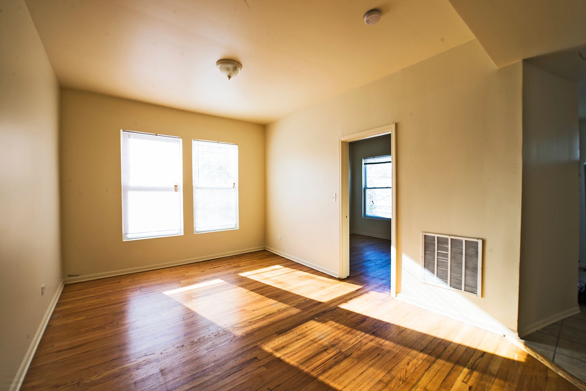 Empty room with hardwood floors, sunlight, windows, and an open doorway.