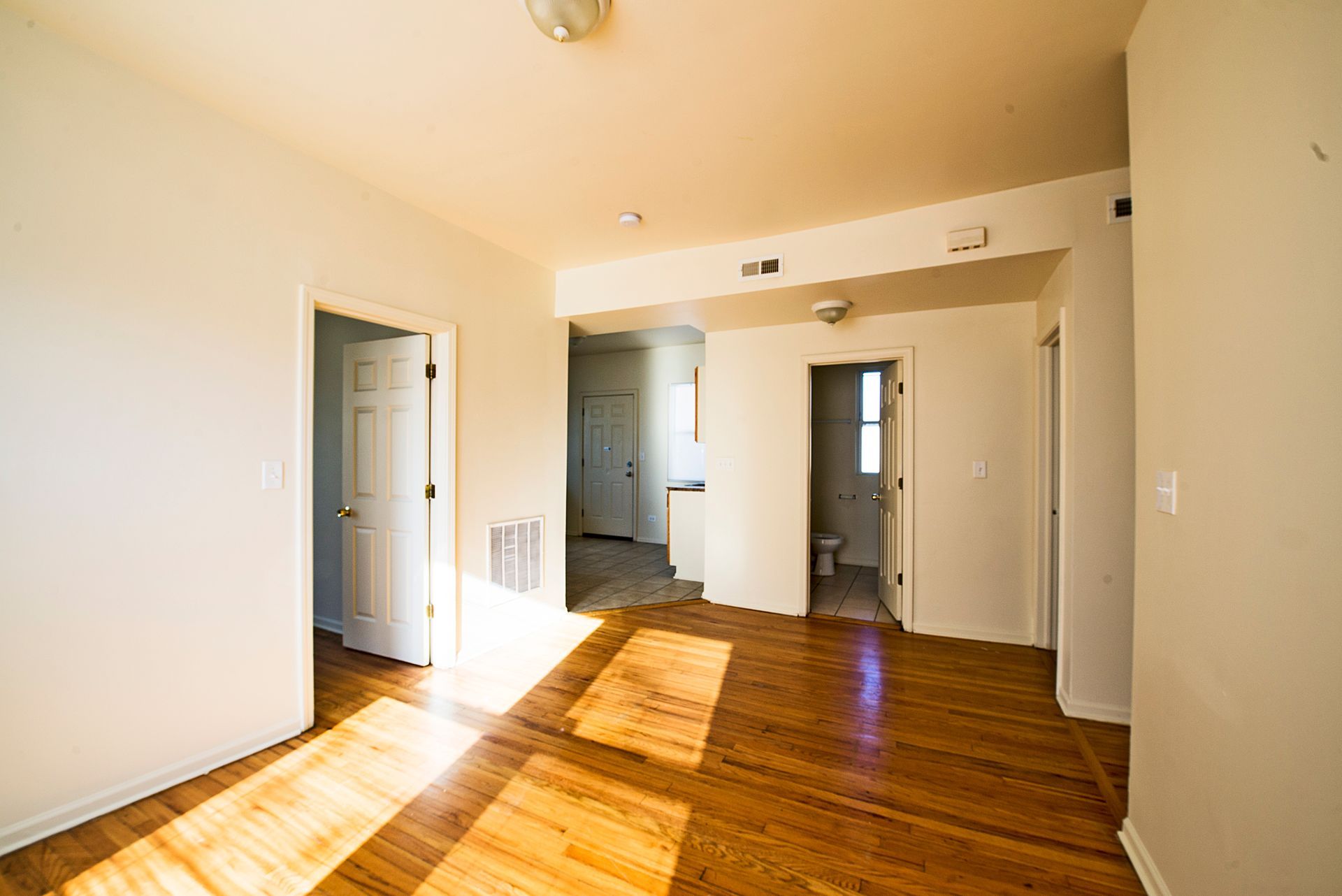 Empty room with wood floors, three white doors, and a small hallway with a bathroom.