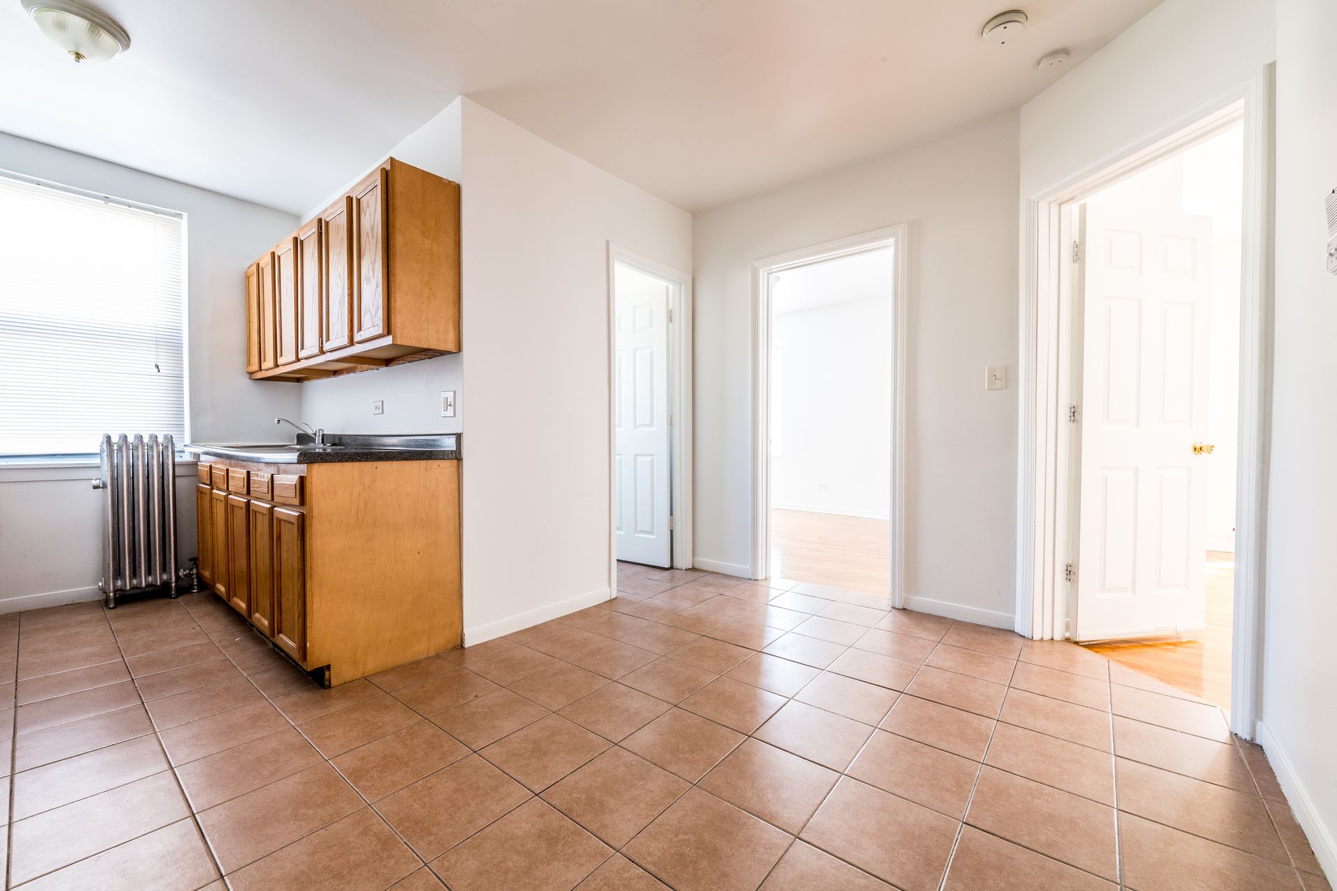 Empty kitchen with wood cabinets, tiled floor, and two doorways.