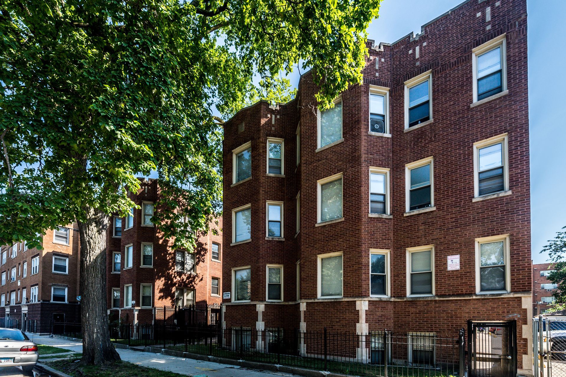 Brick apartment buildings with multiple windows, tree-lined street.