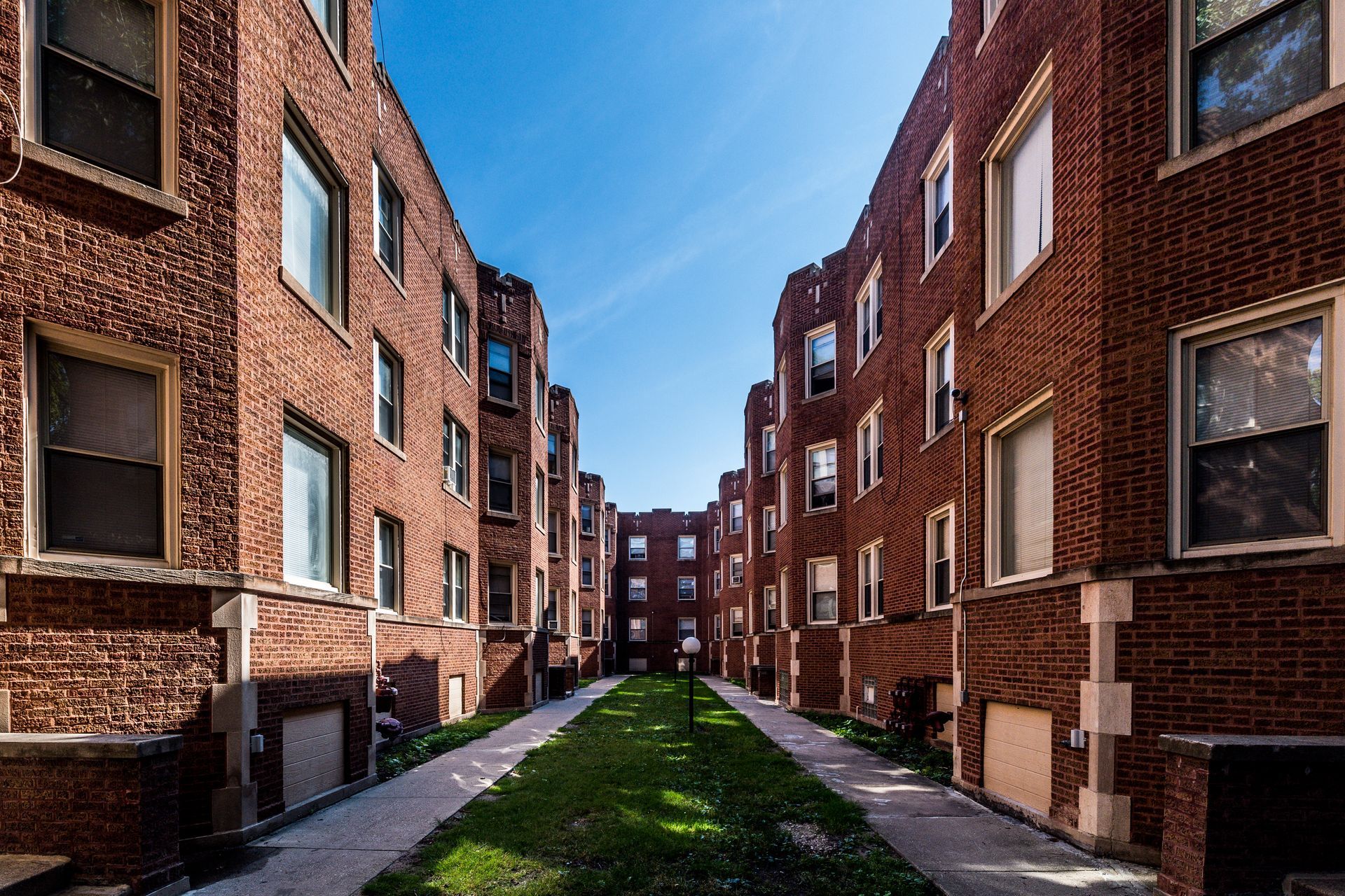 Brick apartment buildings facing each other, a narrow grassy courtyard in between, sunny day.