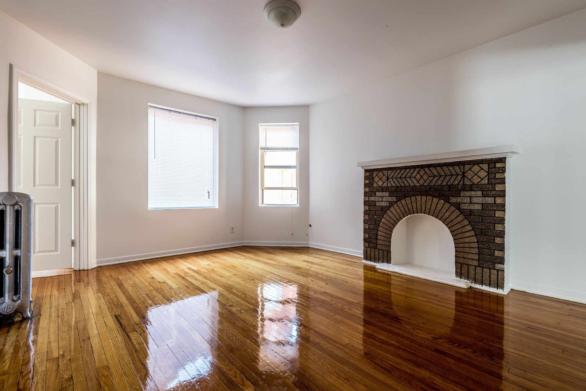 Empty room with hardwood floors, fireplace, two windows, and door.