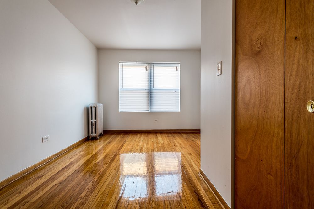 Empty room with hardwood floors, a window, radiator, and a wooden closet door.