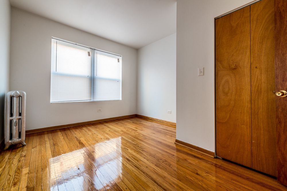 Empty room with hardwood floors, a window, radiator, and wooden closet door.