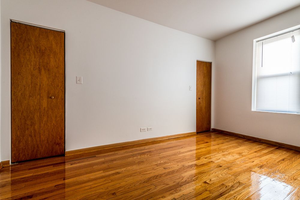 Empty room with hardwood floors, two wooden doors, and a window.