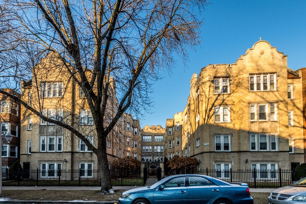 Apartment buildings with ornate facades under a clear sky. A blue car is parked in front.