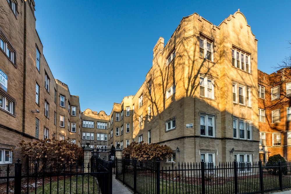 Brick apartment building with black fence and bare trees against blue sky.