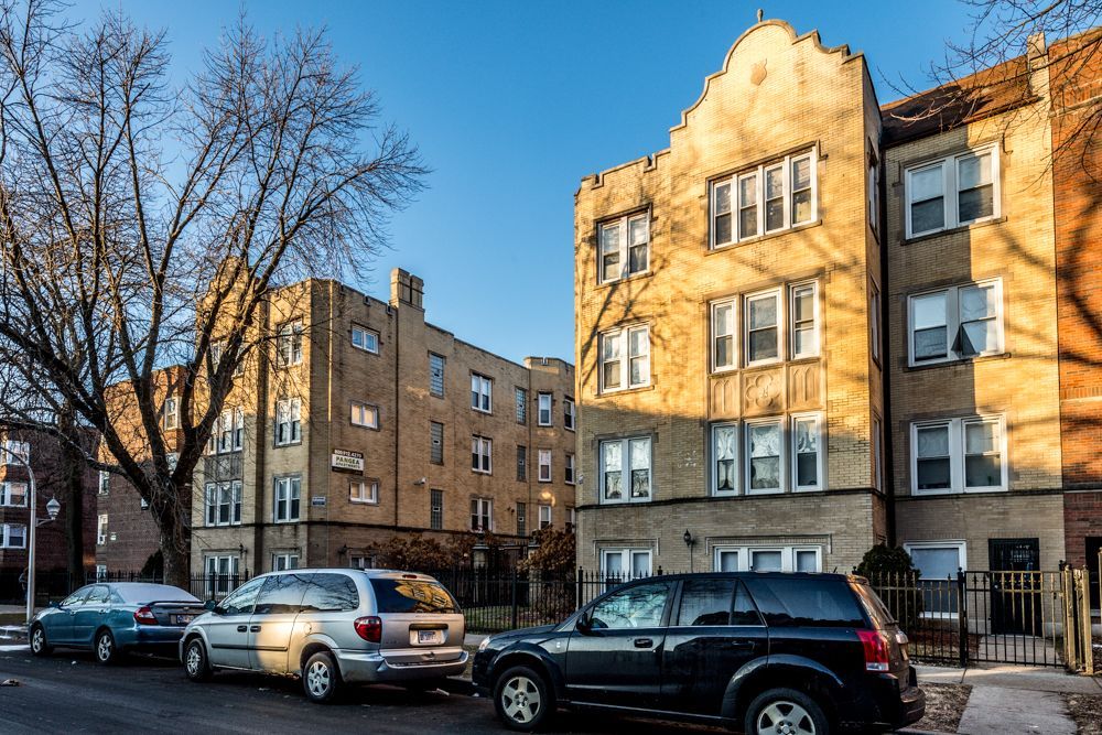 Apartment buildings line a street with parked cars on a sunny day.