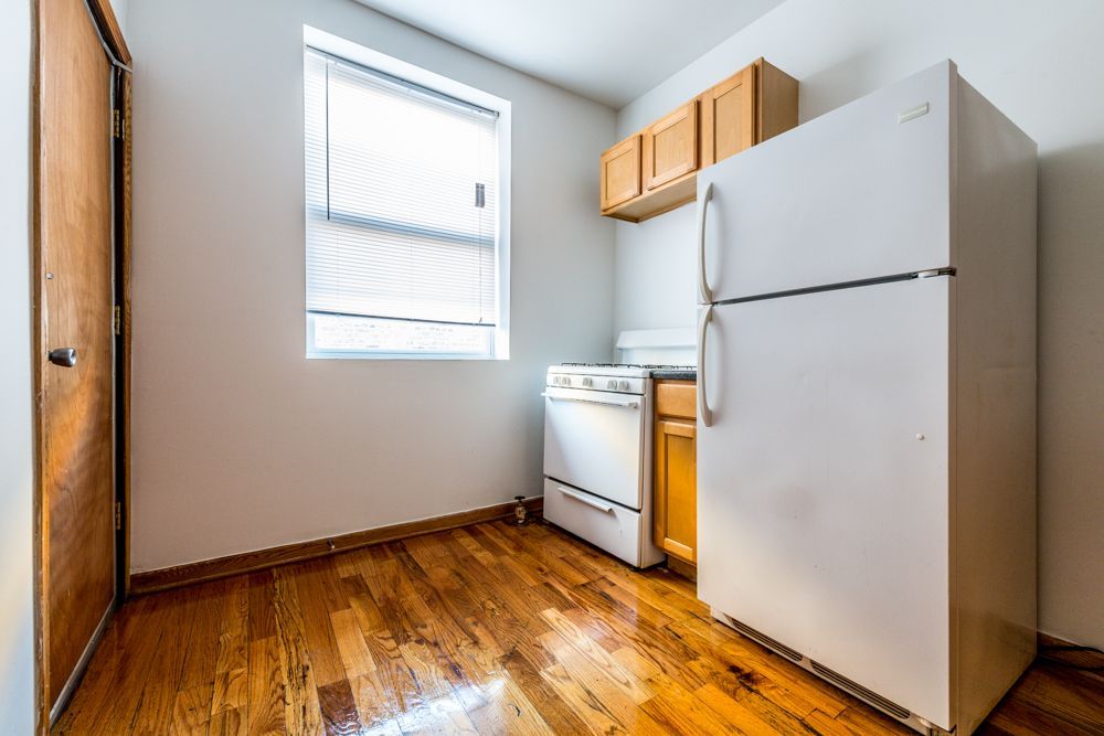 Small kitchen with wood floors, white appliances, small window, and wooden cabinets.