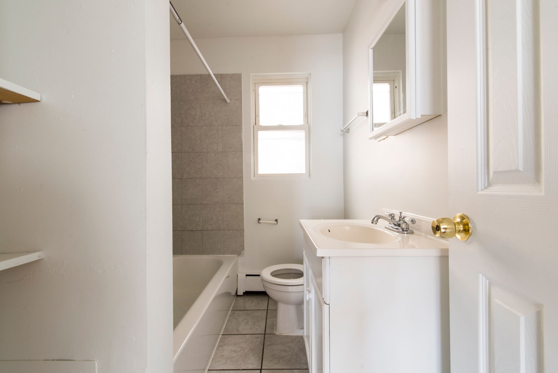 White bathroom with a tub, toilet, sink, mirror, and window.