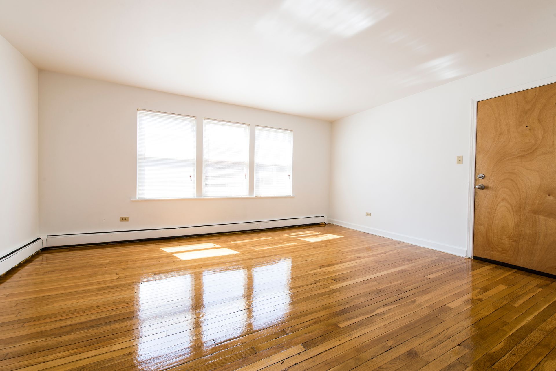 Empty room with hardwood floors, a window, and a closed wooden door.