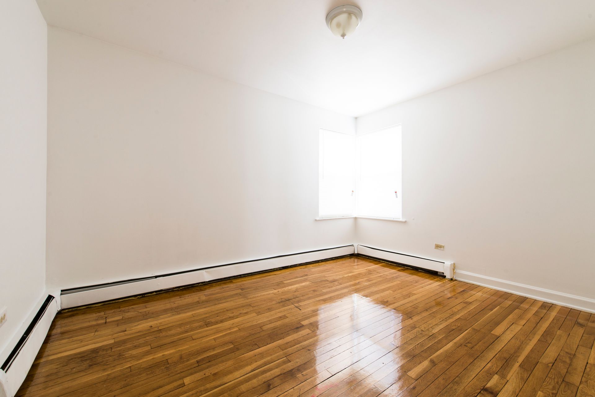 Empty room with hardwood floors, white walls, and a window.