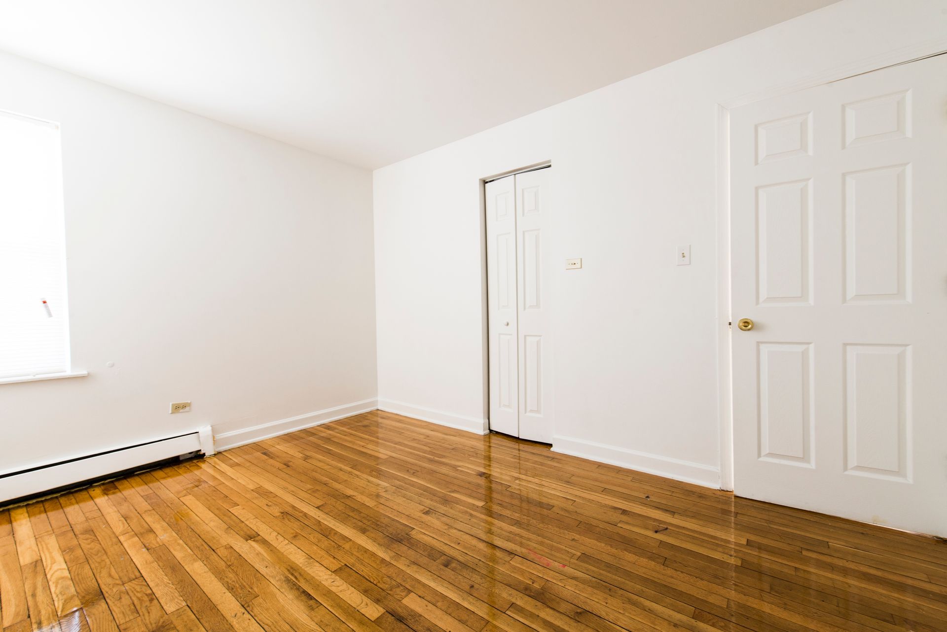 Empty room with hardwood floors, white walls, two white doors, and a window.