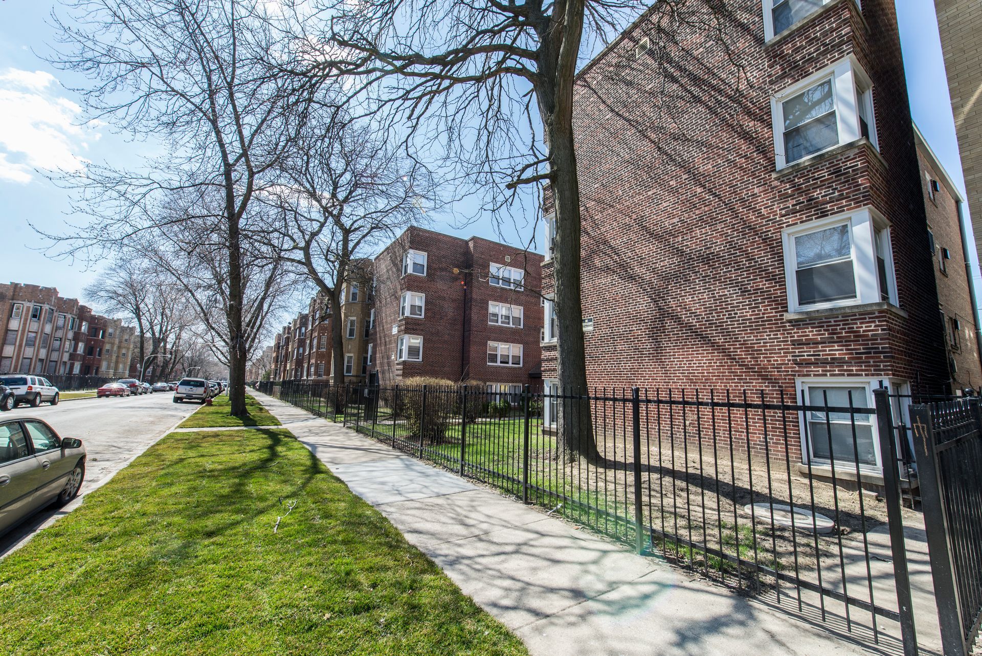 Street view with brick apartment buildings, sidewalk, and trees on a sunny day.