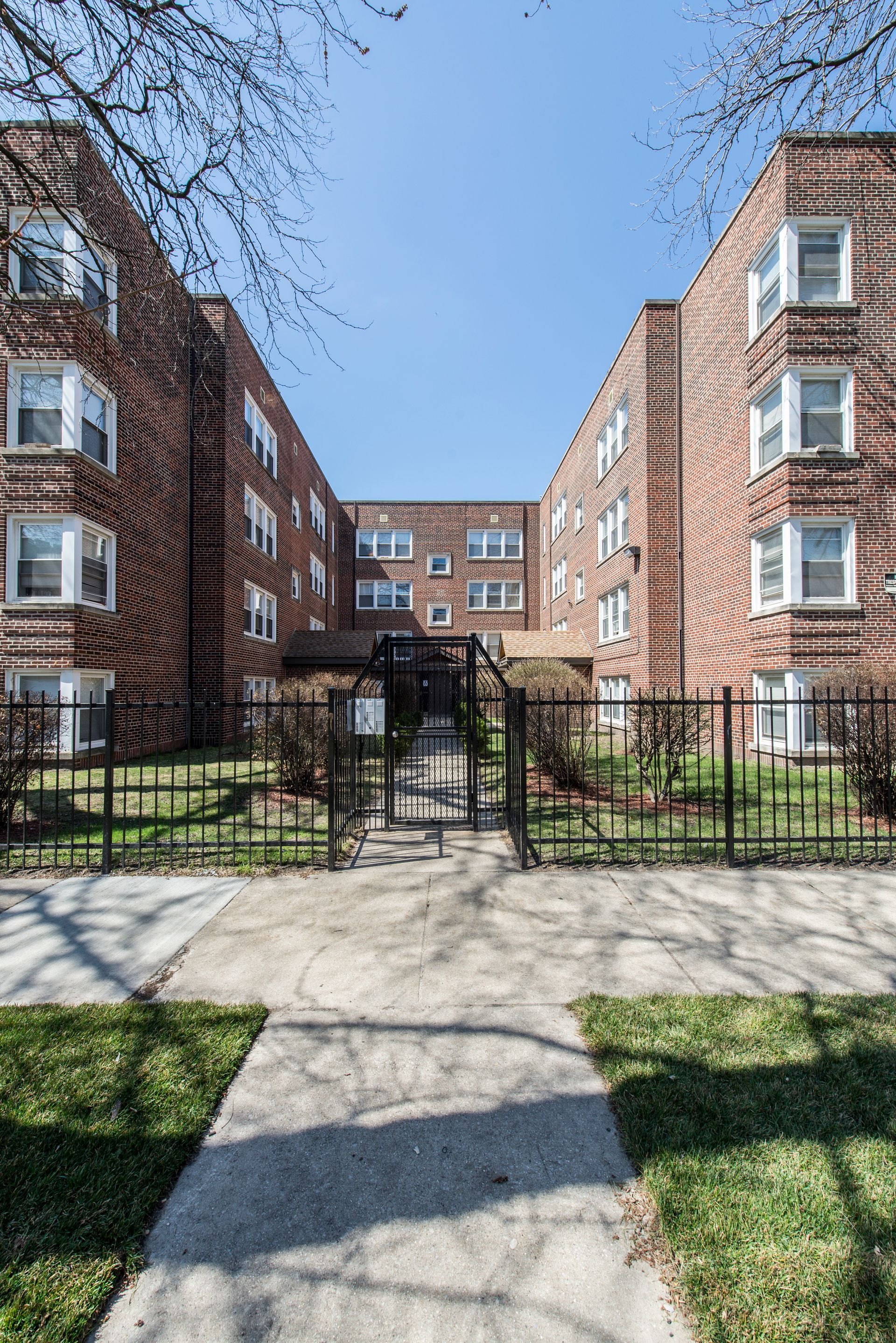 Brick apartment buildings with gated entrance; blue sky.