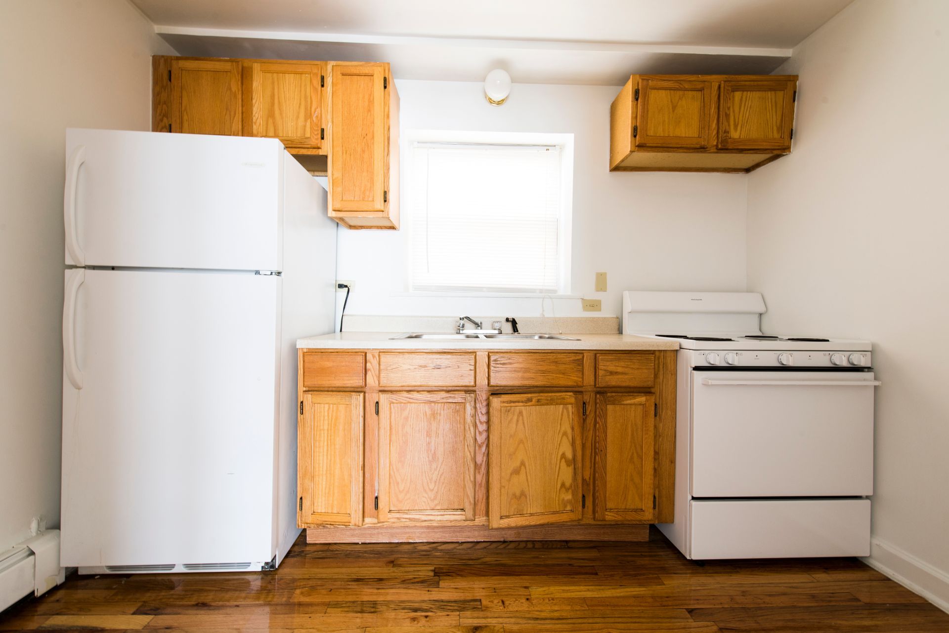 Small kitchen with white appliances, wooden cabinets, and a window.
