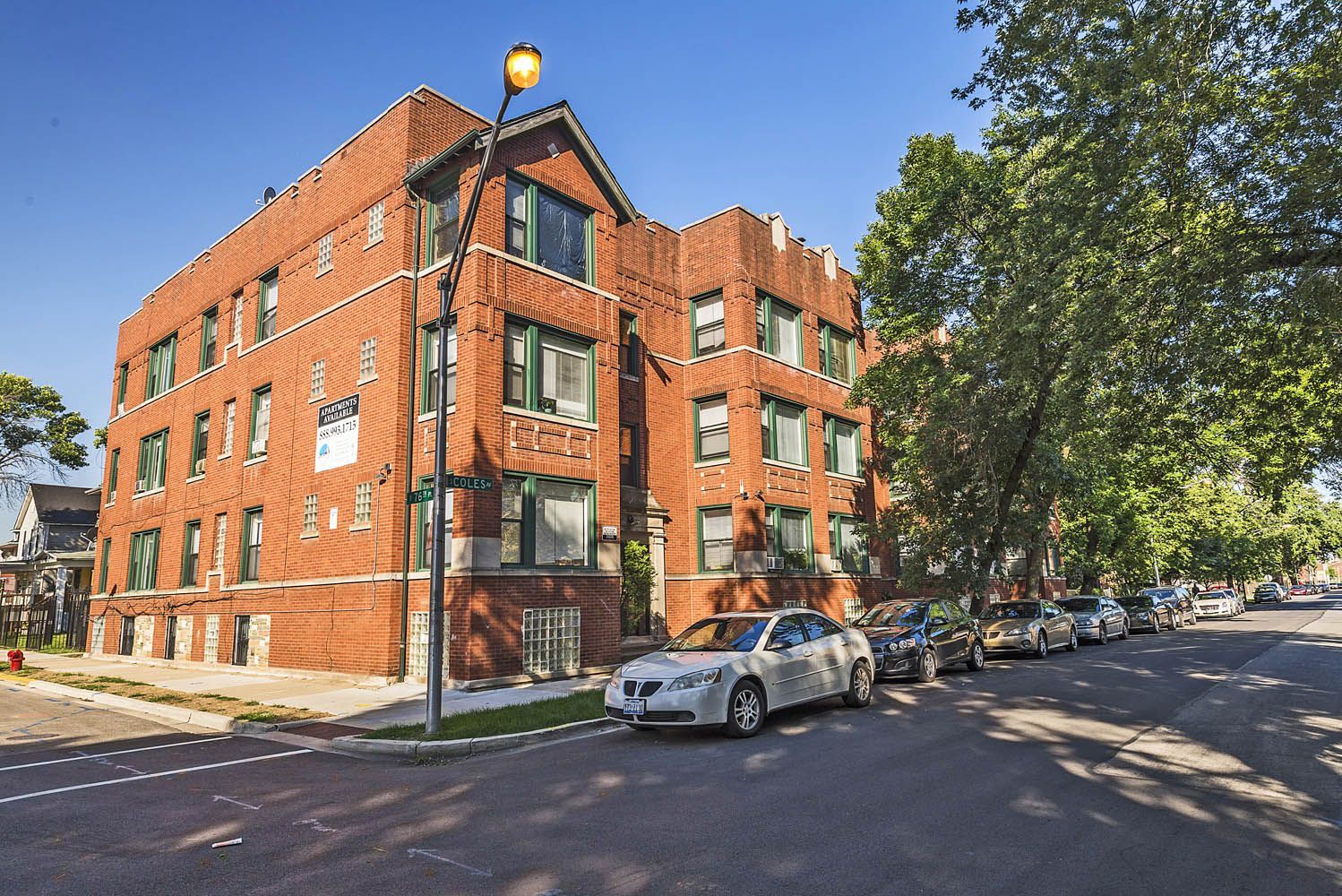 Red brick apartment building on a city street, parked cars, sunny day.