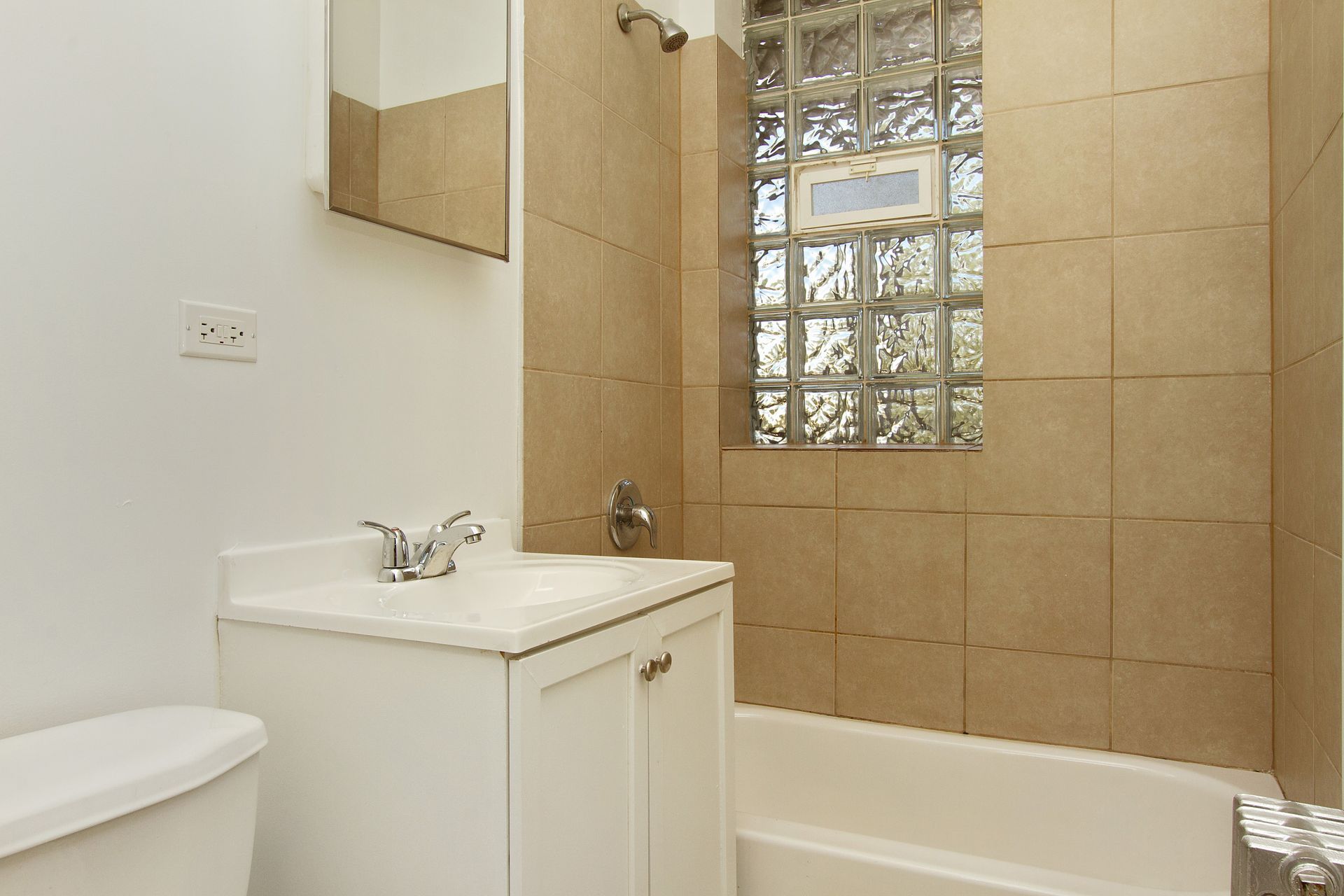 Bathroom with white toilet, vanity, and shower/tub combo with tile walls and a glass block window.