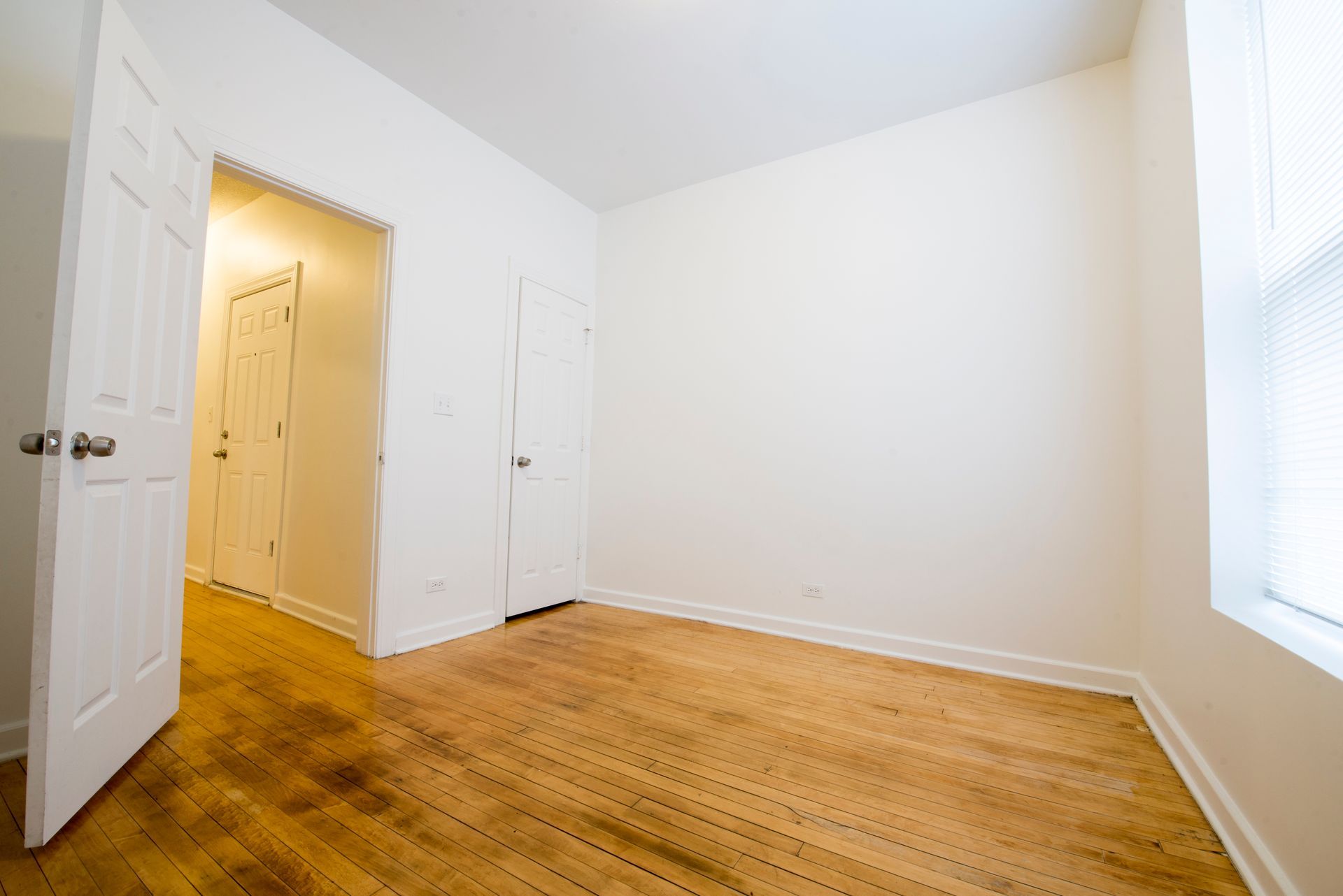 Empty room with hardwood floors, white walls, and a doorway.