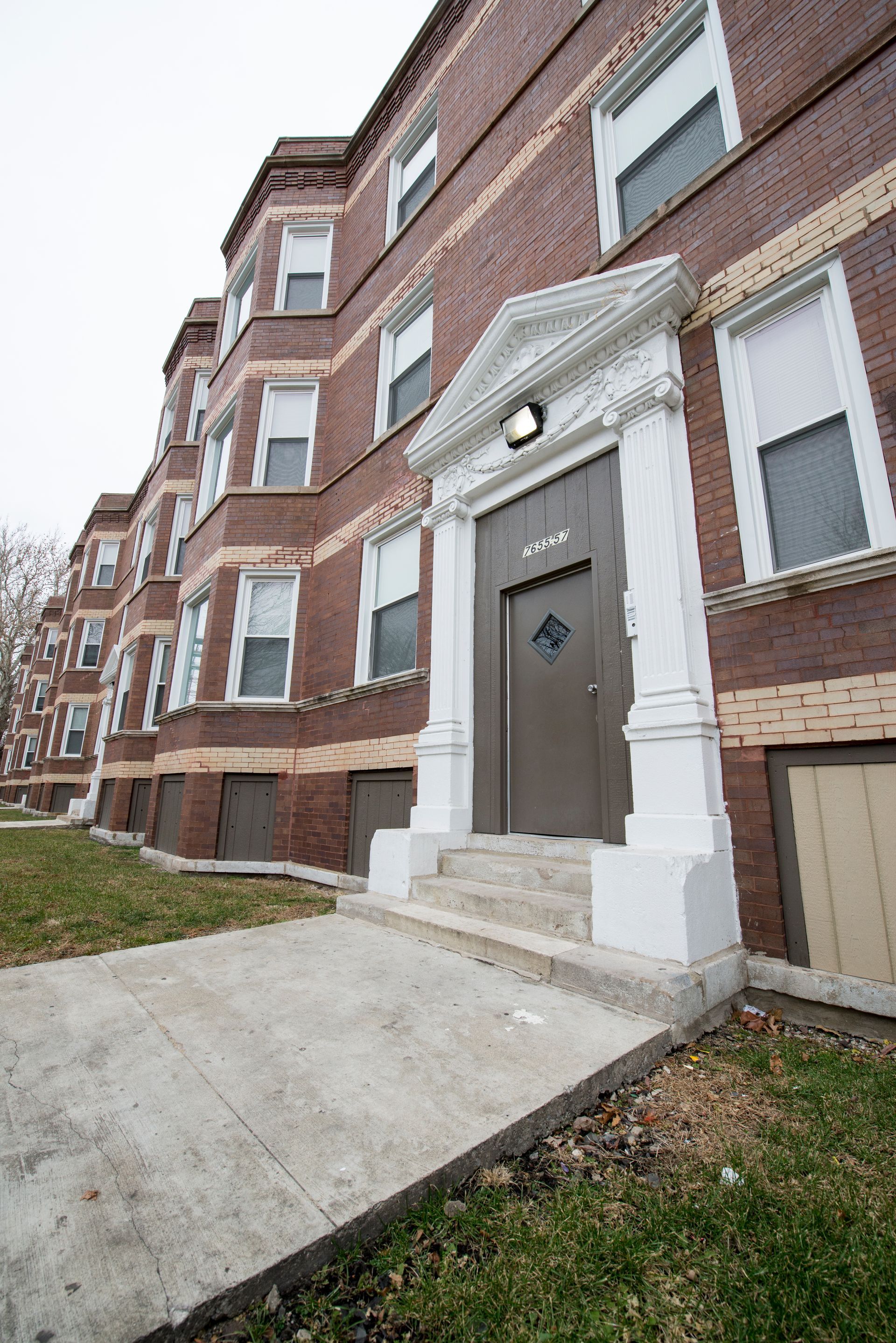 Brick apartment building with white door trim, steps, and concrete path.